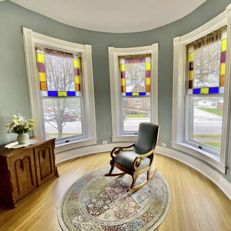 A rocking chair in a lovely green room with curved stained glass windows