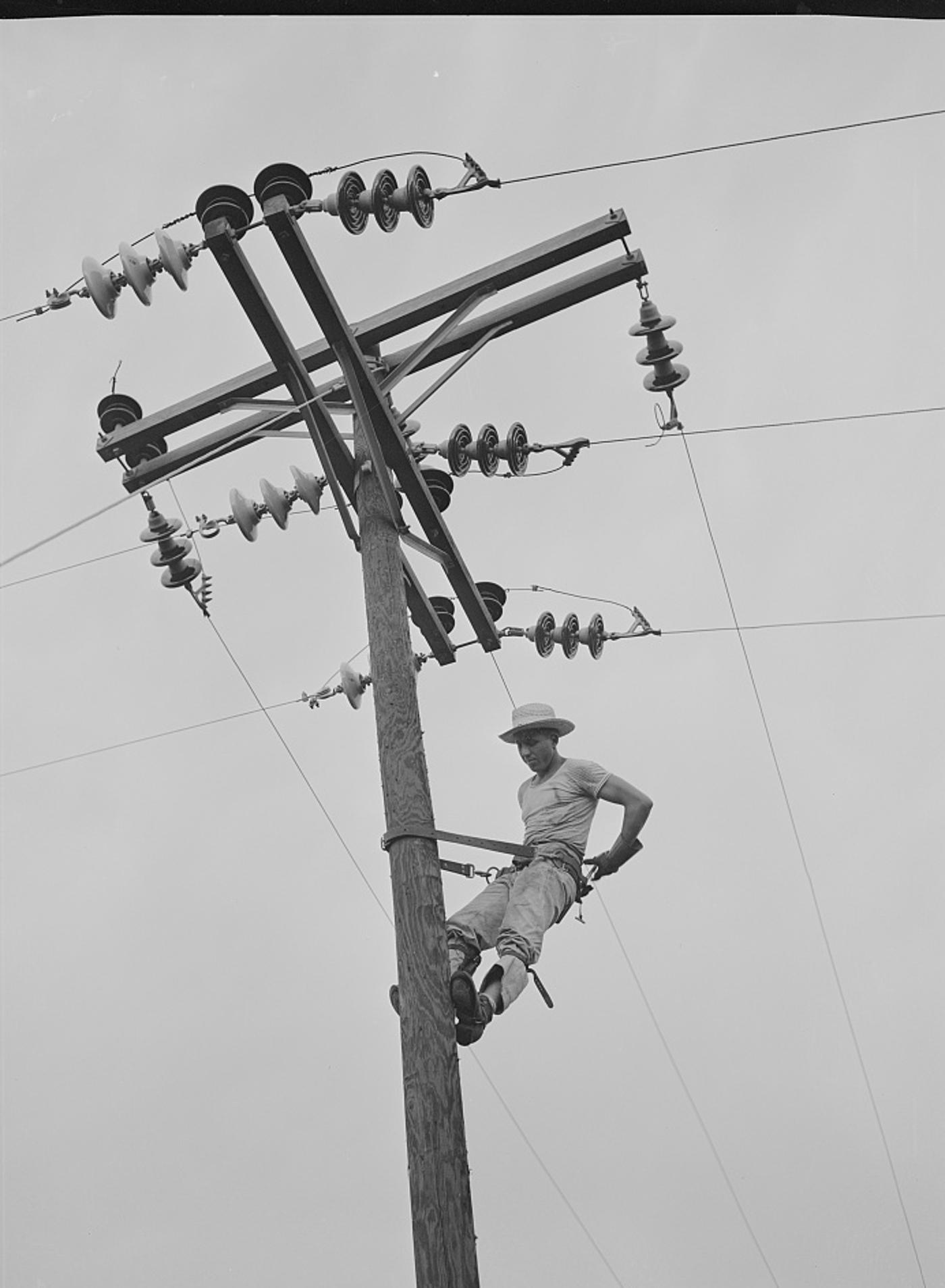 A Rural Electrification Administration cooperative lineman climbing a wooden power pole strung with wires near Hayti, Missouri, in 1942.
