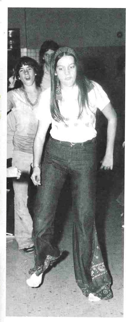 Yearbook photo of a teenage girl dancing in a headband, white T-shirt and wide bell-bottom jeans trimmed with bandana fabric.
